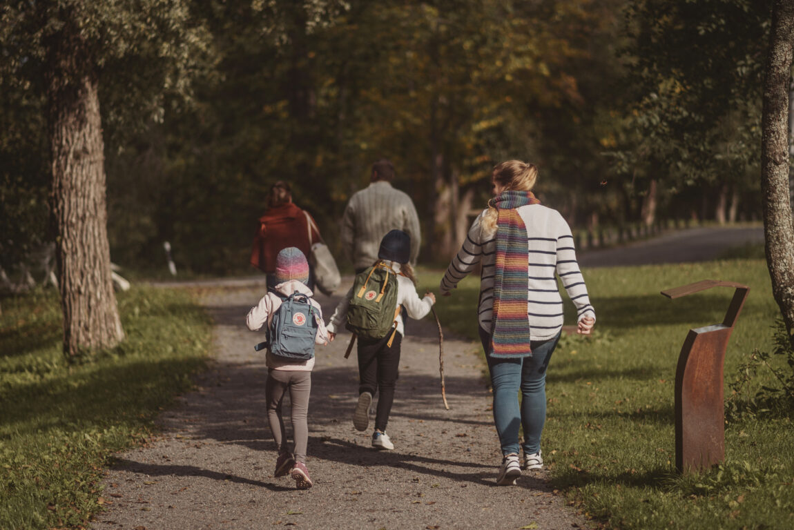 Barnfamilj promenerar längs sandväg.